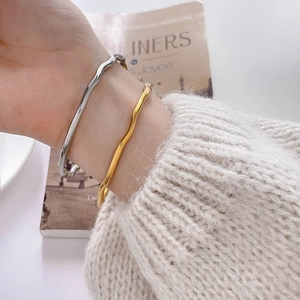 Detailed view of wavy gold and silver minimalist bangles styled with knitwear