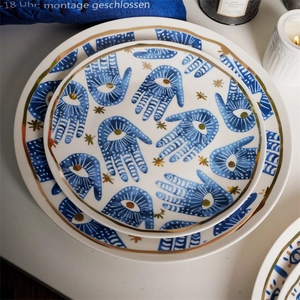 Detail view of white ceramic plates with blue Hamsa Hand patterns and gold edge decor