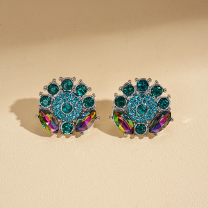 Close-up of geometric flower earrings with green and blue crystals on beige leather