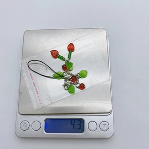 Close-up detail of a handmade cherry beaded phone charm showing 4.3g weight on a scale