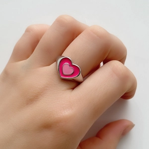 Close-up of a double-layered pink enamel heart ring on a finger with a silver band