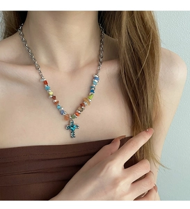 Close-up of a silver cross necklace with blue gemstone and colorful beads on model