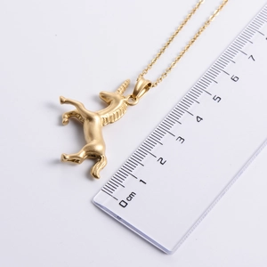 Golden unicorn pendant necklace with sandblasted finish showing 2.5cm size on ruler