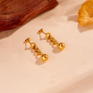 Detail of gold chain drop earrings with spherical bead on a minimalist textured background