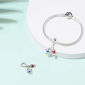 Detailed view of silver snake chain bracelet with artistic hand and red can charms