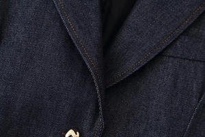 Detalle macro del blazer vaquero azul oscuro con costuras naranjas en contraste y tejido sarga