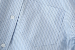 Detailed close-up of light blue striped shirt featuring a chest pocket and white buttons