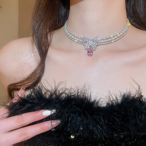 Close-up of elegant silver necklace with pink teardrop gemstone and pearl bow detailing