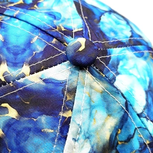 Macro detail of tie-dye baseball cap top button and white stitching on blue fabric