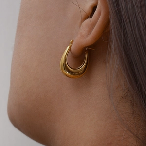 Close-up of a gold-plated hollow U-shaped hoop earring worn by a model in a fashion style
