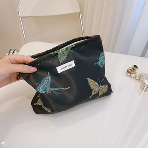 Close-up of black satin makeup bag featuring butterfly embroidery and simple wish label