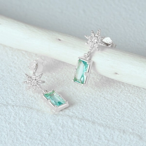 Macro detail of S925 silver earrings with star stud and emerald green rectangular stone