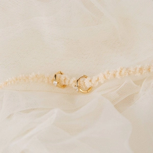 Detail shot of gold-plated hoop earrings with square zircon on soft white mesh background