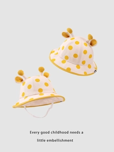 Dettaglio cappello bimbo con corna di giraffa e pois gialli su tessuto beige chiaro