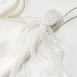 Detail of handcrafted white tulle rose and delicate ribbons on a satin dress strap