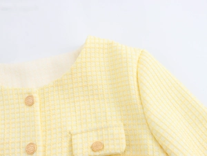 Detailed close-up of yellow tweed jacket collar and gold buttons on textured fabric