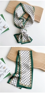 Macro detail of a long silk neck scarf with letter D monogram and green border finish