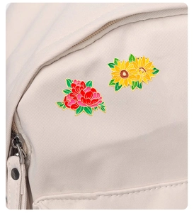 Detailed enamel floral pins with red peony and yellow sunflower on a beige canvas bag