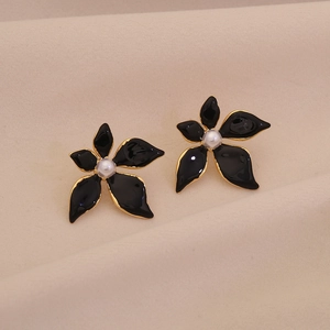 Detail of black enamel flower earrings with gold edges and center pearl on beige fabric