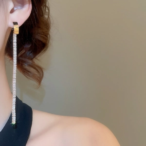 Close-up of elegant gold tassel earrings with zircon stones worn by a model on a warm background