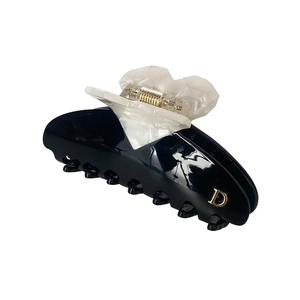 Macro detail of glossy black resin hair claw clip with heart motif and golden D logo