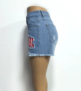 Detail of high-waist light blue denim shorts with distressed rips and red-white patches