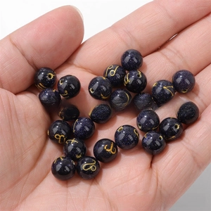 Detail of 10mm blue goldstone beads with gold zodiac signs held in hand for DIY jewelry