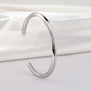 Macro shot of silver C-shaped twisted bangle on a white silk background with soft shadows