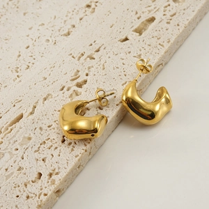 Orecchini a perno spessi in acciaio dorato minimalisti su superficie in pietra beige