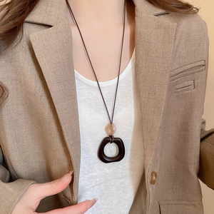 Detail of long resin and wood necklace on model wearing a beige blazer suit