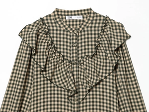 Detail of green and black plaid fabric with ruffled neckline and buttoned long sleeves