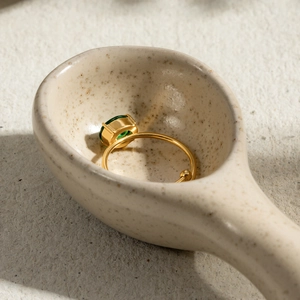 Macro shot of gold-plated adjustable ring with emerald-cut green zircon on ceramic spoon