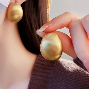 Gros plan de grandes boucles d'oreilles ovales dorées avec texture en métal brossé