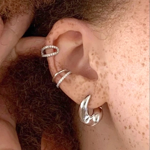 Primo piano di un orecchino a cerchio argento e due ear cuff con zirconi sull'orecchio