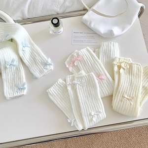 Détail de jambières en tricot côtelé avec rubans en blanc, beige, rose et bleu clair