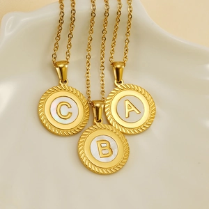 Three 18k gold initial necklaces with white shell round pendants in a ceramic tray