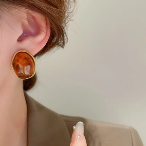 Close-up of irregular resin earrings with amber texture and elegant gold metallic trim
