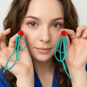 Detailed shot of handmade green beaded tassel earrings with red flower accent on top