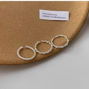 Close-up of three silver adjustable rings with twist and chain textures on a cork tray