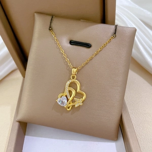 Détail du pendentif cœur doré avec papillon en cristal sur un support à bijoux beige