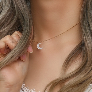 Close-up of a crescent moon pendant necklace with gold beads on a female model