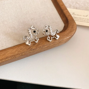 Close-up of silver hollow horse earrings on linen cushion within a wooden tray