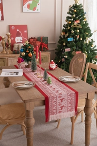Close-up of red Christmas table runner with white reindeer pattern and decorative tassels