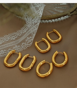 Detailed set of three golden U-shaped and oval hoop earrings on elegant brown silk fabric