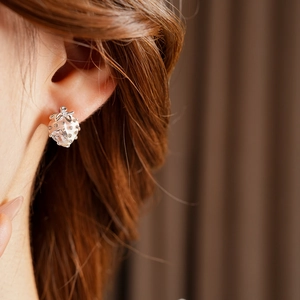 Macro shot of silver strawberry stud earrings with heart-shaped stone on a model ear