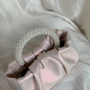 Detail of soft pearlescent beige ruched cloud bag with elegant pearl handle on white silk