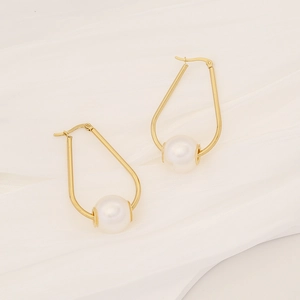 Detail of elegant gold U-shaped earrings featuring a round white pearl on silk fabric