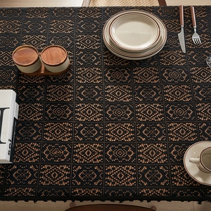 Detail of black and tan woven tablecloth with geometric cutout patterns and tassels