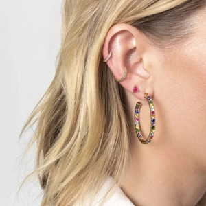 Close-up of a gold large hoop earring with rainbow gemstones worn by a model