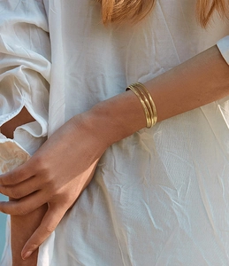 Detail shot of a layered 18K gold-plated open bangle on a model wrist with soft lighting